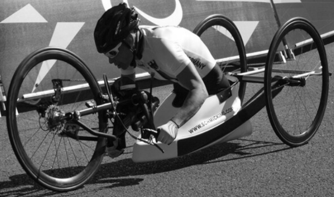 Handbiker in Rennposition mit Helm und Sonnenbrille auf Asphalt